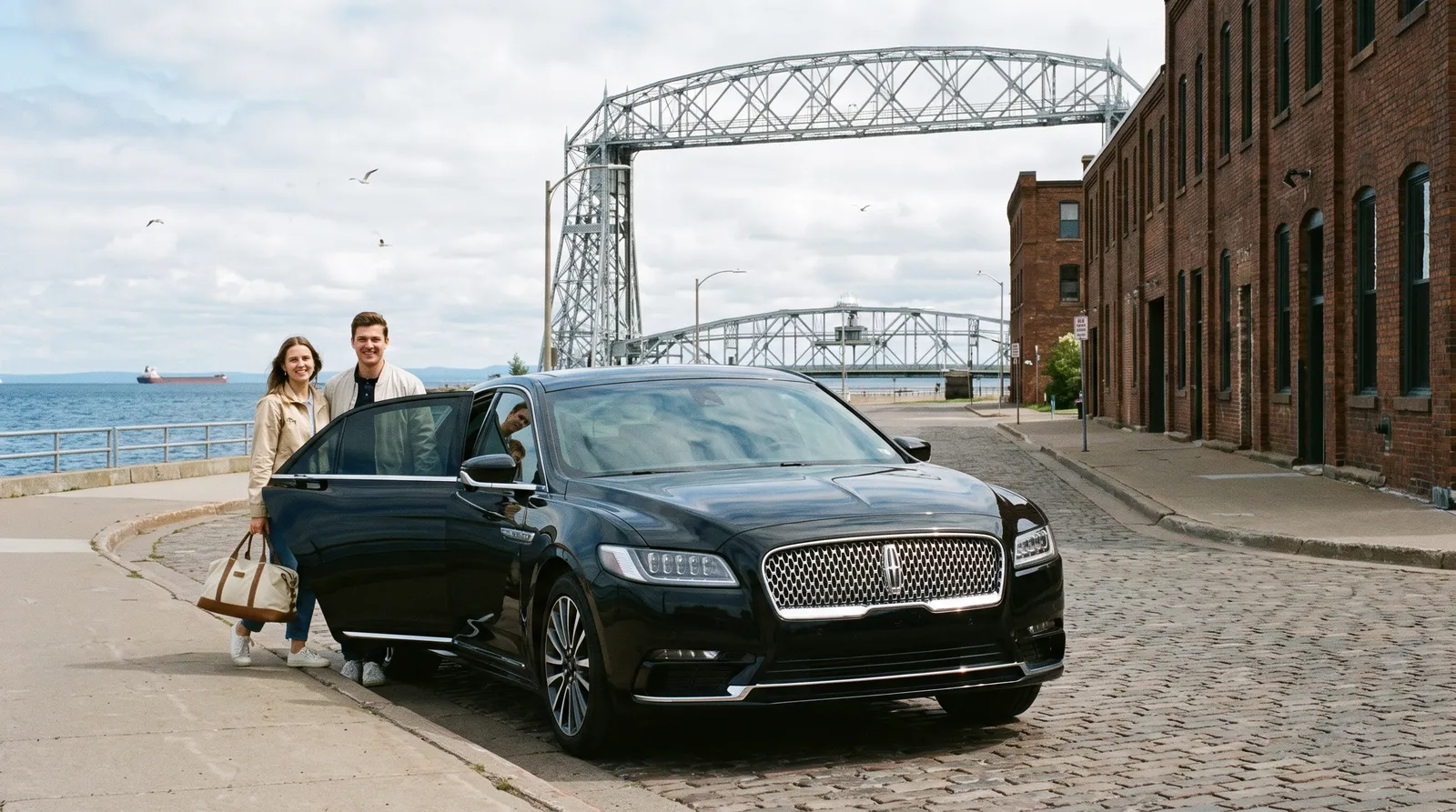 Black Lincoln Continental parked at the curb in Canal Park, Duluth, with the Aerial Lift Bridge and Lake Superior behind
