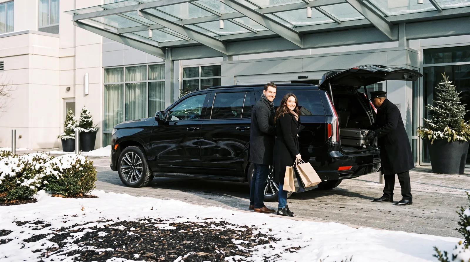 Chauffeur loading shopping bags into the back of a black Cadillac Escalade as a smiling couple steps onto the sidewalk outside a Bloomington hotel near Mall of America